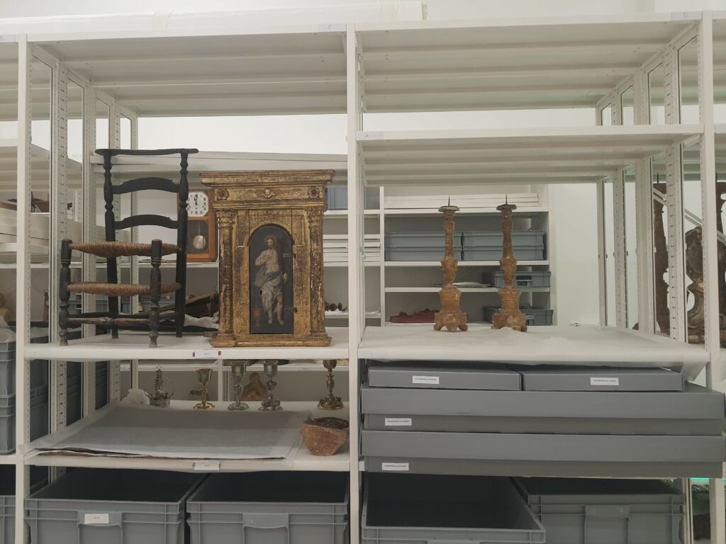 Vue d'une étagère en fer blanc, de face, sur laquelle reposent des objets d'art, tels que des bougeoirs d'église et des tableaux